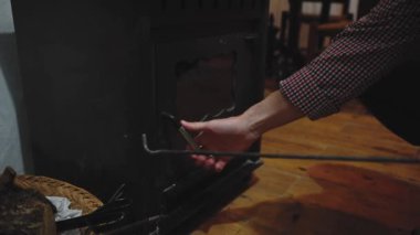 Ağır çekim. Yakın plan bir adam eski metal ahşap sobayı açıyor ve odunları karıştırıyor içinde yanıyor ve ateş yapıyor, kır evini ısıtıyor. - İnsanlar. Kırsal yaşam tarzı. Enerji. Yakıt ve ısıtma