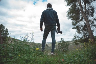 Profesyonel dijital fotoğraf makinesi tutan gezgin bir adamın tam boy portresi, ilkbaharın başlarında yürüyüş yaparken dağlara hayran.