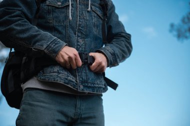 Yakın plan erkek gezgin, doğa yürüyüşü sırasında sırt çantasına bağlanmış, mavi gökyüzü arka planına karşı dağlarda duruyor.