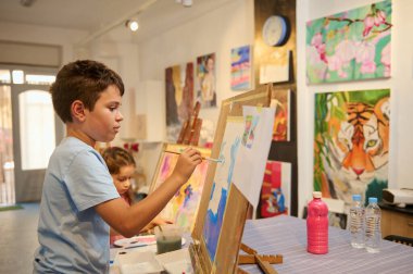 Yetenekli ilkokul çocuğu yaratıcı sanat sınıfındaki tuvale resim çizmeye odaklanıyor. Görsel sanat. Çocukların sanatsal becerilerinin gelişimi.