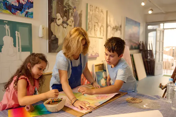 在创意视觉艺术工作坊的艺术课上 受启发的画家女士教孩子在画布上绘画 与可爱的学习者分享建议和技巧 开发创造力 想象力 图库照片
