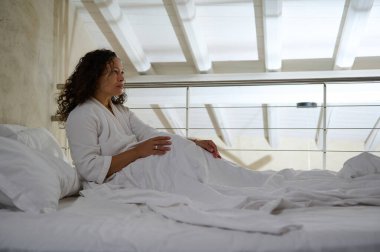 Çok ırklı, kıvırcık, güzel genç bir kadın yatakta uzanıyor. Hafta sonunun keyfini çıkarırken uyanıyor. Beyaz gözleme bornozlu, beyaz çarşaflarda dinlenen hoş, çekici bir kadın.