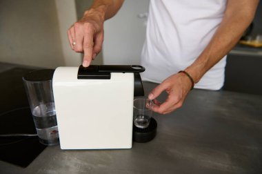 Ev kullanımı için bir kapsül kahve makinesine odaklan ve adam kahvaltı için taze sabah kahvesi hazırlıyor, mutfak tezgahının yanında duruyor. İtalyan yaşam tarzı ve kültürü.