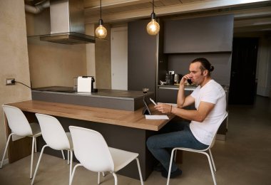 Cep telefonuyla konuşan genç bir adam faturaları ödemenin masraflarını ve masraflarını analiz ederken elinde belgelerle evde oturuyor. Maliye ve ev yönetimi kavramı, planlama bütçesi.