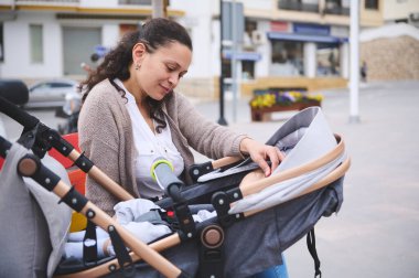 Genç ve güzel bir kadın yeni doğmuş çocuğuyla birlikte bebek arabasında mutlu bir doğum izninin tadını çıkarıyor. Sevecen anne, bebek arabasında bebeğine hayranlık duyarken parkta bankta oturuyor.