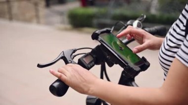 Yakın plan kadın yeşil renkli cep telefonu kullanıyor. Dokunmatik ekranı var. Cep telefonunda kiralık bir uygulamayla elektrikli bisiklet kiralıyor. Bisikletle şehir servisini paylaşıyoruz. Dayanıklılık. Toplu eko taşımacılığı