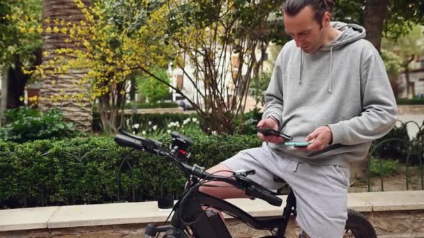 Белый Молодой Человек Смартфоном Руках Арендует Электрический Велосипед Помощью Приложения — стоковое видео