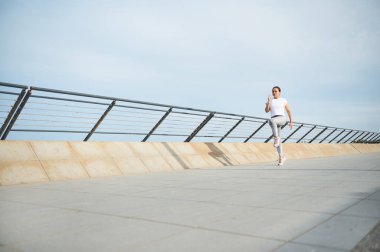 Şehir sokaklarında koşan genç bir atletik kadının tam boy portresi. Mutlu bayan koşucu kalori yakıyor, sabah gezinti güvertesinde koşuyor. - İnsanlar. Spor. Aktif sağlıklı yaşam tarzı.
