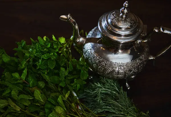 A silver teapot and a bunch of fresh green mint on the foreground. Traditional Moroccan tea as symbol of the hospitality of Moroccan people. Selective focus. Moroccan tea a la menthe. Overhead view