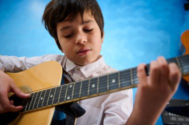 Yakın plan beyaz, kendine güvenen genç çocuk gitarını zevkle tıngırdatırken telleri koparıyor. Akustik gitar çalan genç çocuktan esinlendim. Müzik dersinde gitar öğrenen bir çocuk.