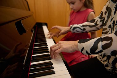 Yakın plan kadın piyanist piyano klavyesinde el ele tutuşuyor, siyah beyaz tuşlara dokunuyor, küçük kız öğrencisine müzik dersi verirken klasik melodi oluşturuyor. - İnsanlar. Sanat ve hobiler