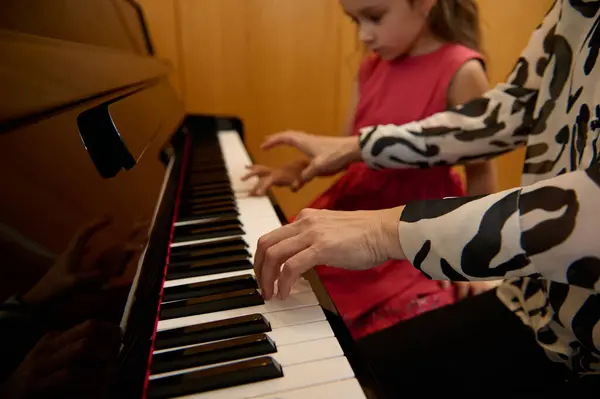 Close-up woman pianist holding hands on piano keyboard, touching black and white keys, preforming classical melody during while giving music lesson to her little student girl. People. Arts and hobbies