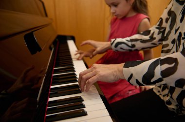 Yakın plan kadın piyanist piyano klavyesinde el ele tutuşuyor, siyah beyaz tuşlara dokunuyor, küçük kız öğrencisine müzik dersi verirken klasik melodi oluşturuyor. - İnsanlar. Sanat ve hobiler