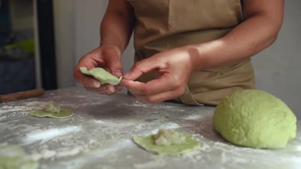 一位穿着米黄色围裙的女厨师的手上拿着融化的菠菜用绿色面团做饺子 然后用土豆泥填满饺子的细节 她站在农舍的厨房桌旁 — 图库视频影像