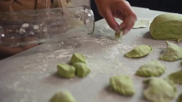 家庭主妇的特写镜头 用玻璃瓶做滚针 用绿色菠菜面团做饺子 站在厨房餐桌旁 在农村家庭厨房里撒些面粉 — 图库视频影像