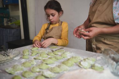 Kafkas çocuk portresi mutfakta annesine yardım ediyor, hamur işlerini dolduruyor, un masasında duruyor. Anne ve kızı evde aile yemeği için Varennyky pişiriyor..