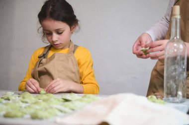 Çocuklar yemek kursunda hamur tatlısı yapmayı öğrenirler. Geleneksel Ukrayna tarifine göre ev yapımı Varennyky hazırlıyorum. Yakından küçük bir kız çocuğu hamur köftesi yontuyor, un kaplı masada duruyor.