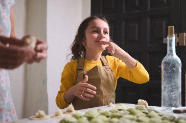 Kafkas tapılası, bej önlüklü küçük yaramaz kız. Annesiyle mutfakta hamur köftesi pişirirken patates püresi yerken gülümsüyor..