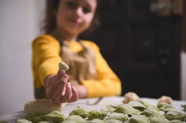 Bulanık bir kızın eli, bej önlüklü küçük şef, kameraya ev yapımı bir hamur tatlısı uzatır, kameraya gülümser, un kaplı bir masada mantı, pelmeni, vareniki...