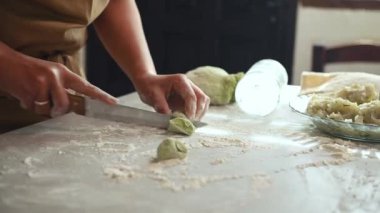Yakın plan kadın yeşil ıspanak hamurundan sosis kesiyor ve köy mutfağında ravioli hazırlıyor, mermer masada taze malzemelerle duruyor.