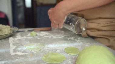 Bej önlüklü kadının elleri, hamuru yeşil ıspanakla sarmak için cam şarap şişesi kullanıyor, geleneksel Ukrayna Varennyky 'sini patates püresiyle pişiriyor. Yiyecekler. Gelenekler. Kültür