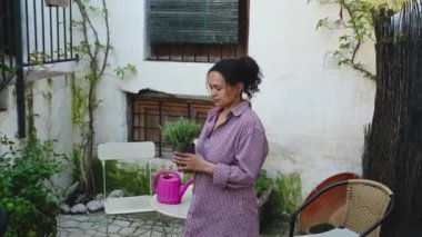 Kadın bahçıvan elinde tuttuğu lavanta bitkisinin kokusunu kokluyor, kır evinin arka bahçesinde duruyor. - İnsanlar. Kırsal yaşam tarzı. Bahçıvanlık. Bahçecilik. Çiçekçilik