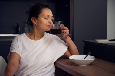 Beyaz pijamalı genç bir kadının yakın plan portresi. Mutfak masasında gözleri kapalı oturmuş yeni demlenmiş espresso kahveden yudumluyor. - İnsanlar. Ev hayatı işte. Hobiler ve eğlence.