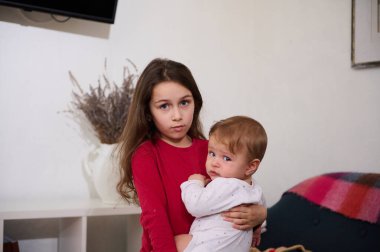 Küçük erkek kardeşine evde sarılan tatlı bir kız çocuğu. Aile ilişkileri ve bakım kavramı. Uluslararası Çocuk Günü. Ağabey ve kız kardeş birlikte