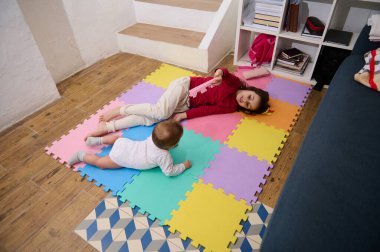 Yukarıdan kardeşlerin evdeki yapboz halısında birlikte oynadığı manzara. Sevimli küçük bir kız, 6 aylık bir erkek bebek olan erkek kardeşiyle ilgileniyor. Mutlu aile kavramı