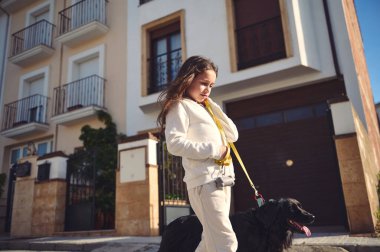 Avrupalı sevimli küçük kız köpeğini güneşli bir günde beyaz spor giyim kuşamlarıyla şehir sokaklarında gezintiye çıkarıyor. Tatlı çocuk cocker spanyel 'ini dışarıda gezdiriyor.