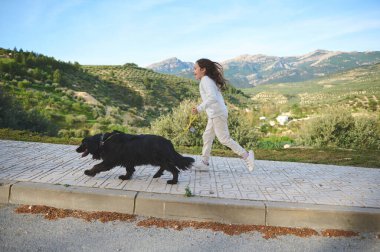 Doğada köpeğini tasmayla gezdirirken 6 yıl satılan beyaz bir kızın tam boy yan portresi. - İnsanlar. Doğa. Evcil hayvanlar. Evcil hayvan oyunu
