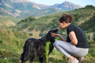 Sevecen genç bir kadın, yoldaş köpeğiyle konuşuyor, dağlarda doğa yürüyüşü yaparken soylu siyah cocker spaniel hayvanını kucaklıyor. Evcil hayvan ve insan konsepti