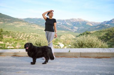 Spor giyim sektöründe genç ve güzel bir kadın köpeğini doğada gezdirirken safkan siyah cocker köpeğiyle dağlarda doğa yürüyüşünün keyfini çıkarıyor.