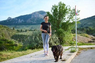 Spor kıyafetli mutlu bir kadın köpeğini tasmayla dolaştırıyor. Güzel bir dişi, safkan cocker spaniel 'iyle dağlarda yürümeyi sever. Evcil hayvan, insan ve hayvan oynuyorlar.