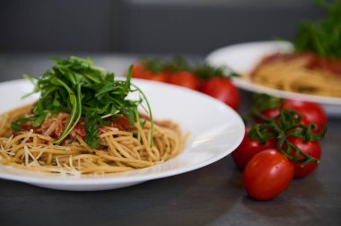 Domates soslu İtalyan spagetti capellini, parmesan peyniri ve roka yaprağı. Mutfak masasında taze olgun organik domates vişnesi..