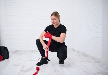 Boks eldivenlerini boks antrenmanına hazırlamadan önce beyaz, kendine güvenen, siyah spor giyen kadın dövüşçünün tam boy fotoğrafı. Dövüş sanatı ve dövüş konsepti. Üst görünüm