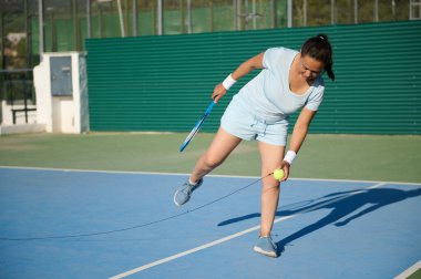 Kendine güvenen 40 'lı yaşlarda, açık sahada aktif olarak tenis oynayan bir kadın. Açık mavi kıyafetli, forehand salıncaktaki yeteneğini gösteriyor. Odaklanmış ifade spora olan bağlılığını vurguluyor