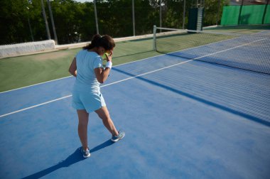 Parlak ve güneşli bir günde tenis oynayan orta yaşlı bir kadın. Tenisçi sahada hazır bir duruş sergileyerek, odaklanmayı ve atletizmi gösteriyor..
