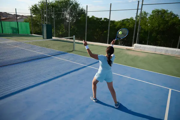 40 'lı yaşlarda, dışarıda tenis oynayan, oyununa odaklanan ve raketiyle topa vurmaya hazırlanan kararlı bir kadın. Güneşli hava, canlı atmosferi güçlendirir..