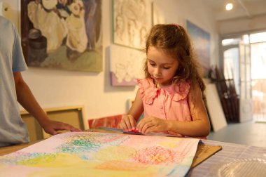 Çocuklar resim dersi alıyor, resim yapıyor, atölyede öğretmenle resim yapıyor. Yaratıcı bir ortamda renkli sanat eserlerine odaklanan genç bir kız..