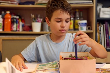 Resim dersinde renkli kalemlerle resim çizen çocuk, sanat çalışmalarına odaklanıyor..