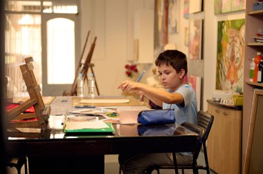 Çocuklar resim dersi alıyor, resim yapıyor, atölyede öğretmenle resim yapıyor. Genç çocuk yaratıcı bir sınıf ortamında sanat eserlerine odaklanmış..