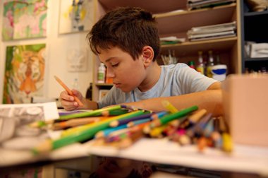 Çocuklar resim dersi alıyor, resim yapıyor, atölyede öğretmenle resim yapıyor. Genç bir çocuk yaratıcı bir stüdyo ortamında renkli kalemlerle çizim yapıyor..