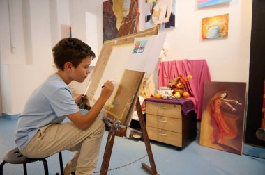 Resim dersi alan bir çocuk, atölyede öğretmeniyle tuvale resim çizip resim yapıyor. Yaratıcılık ve renkli sanat eserleriyle dolu canlı bir stüdyo..