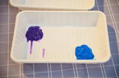 Mor ve mavi boya içeren beyaz boya tepsisinin yakın çekim görüntüsü, sanat sınıfında kullanılmaya hazır, çizim ya da resim atölyesinde.