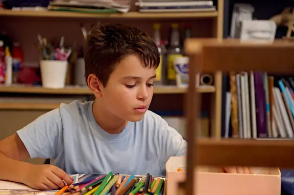 stock image Kids have art class, drawing, painting with teacher in workshop. Young boy concentrating on his artwork surrounded by colored pencils and other art supplies.