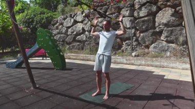 Güneşli bir yaz gününde 40 'lı yaşlarındaki bir adam spor yaparken spor yaparken spor yaparken ağırlık kaldırıyor. Antrenmanına odaklanmış ve gücünü ve sağlığını geliştirmeye kararlı..