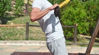 40 'lı yaşlarında bir adam açık hava eğitim parkında çalışıyor. Kollarını ve vücudunun üst kısmını güçlendirmek için süspansiyon kayışları kullanıyor. Bu videonun sağlıklı, aktif ve motive edici bir hissi var..