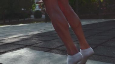 Gri şort ve beyaz çorap giyen bir adam parkta yeşil yoga minderinde baldır kaldırıyor. Bu fitness videosu egzersiz ve fiziksel refahın önemini vurgular..