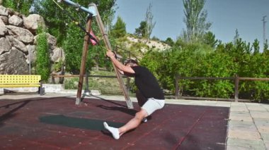 Formda bir adam güneşli bir yaz gününde dışarıda parktadır. Vücut çalışmasını tamamlamak için spor aletlerini kullanıyor. Bacaklarını, karnını ve kollarını çalıştırıyor..